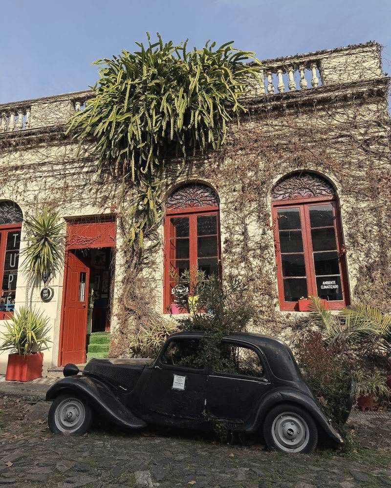 Altes Haus mit roten Fensterläden und einem schwarzen Oldtimer davor