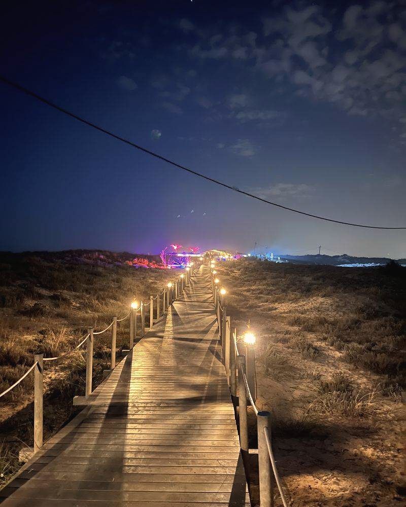 Beleuchteter Holzsteg durch Dünen bei Nacht